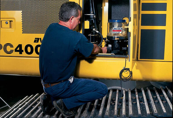 L'immagine mostra un uomo accovacciato davanti a un sistema di lubrificazione